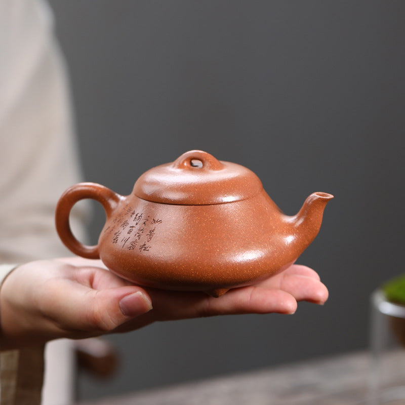 Reverse of the Pine Wind Yixing teapot held in one palm, hand-carved with a line of calligraphy