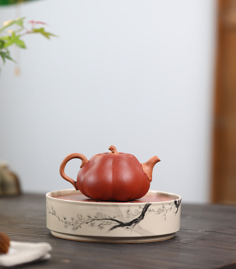 The Pumpkin Yixing clay teapot on a porcelain tea tray with a plum blossom design, handle to the left