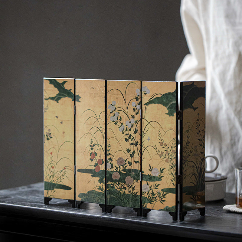 Gold Meadow mini folding screen, front, standing on a tea table with a person in white linen behind