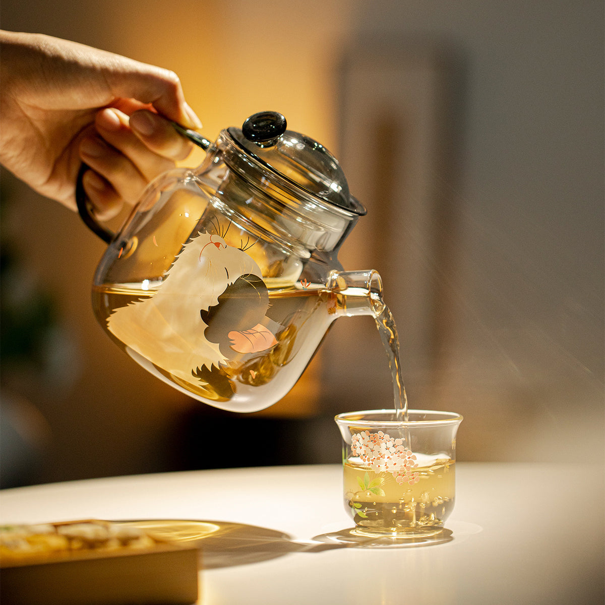 Pouring tea from the cat and butterfly glass teapot into a small glass cup