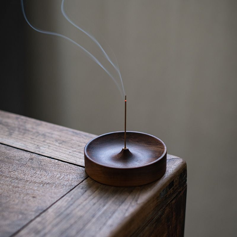 Walnut incense holder with a lit incense stick on a timber table