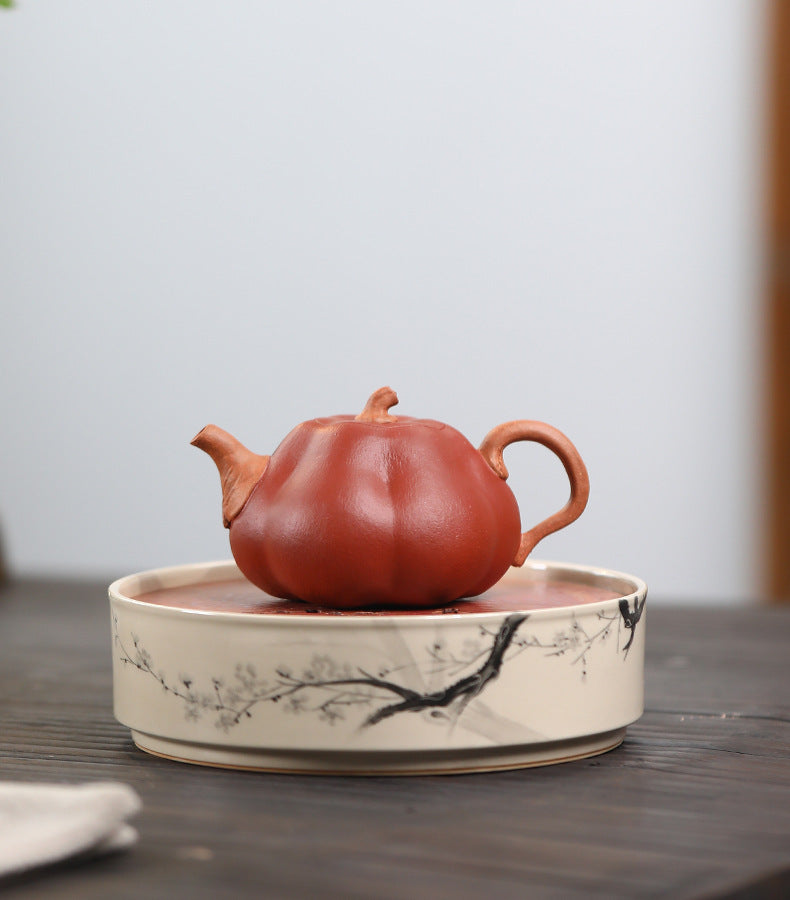 The Pumpkin Yixing clay teapot on a white porcelain tea tray, spout to the left, showing the segmented pumpkin body and inset lid