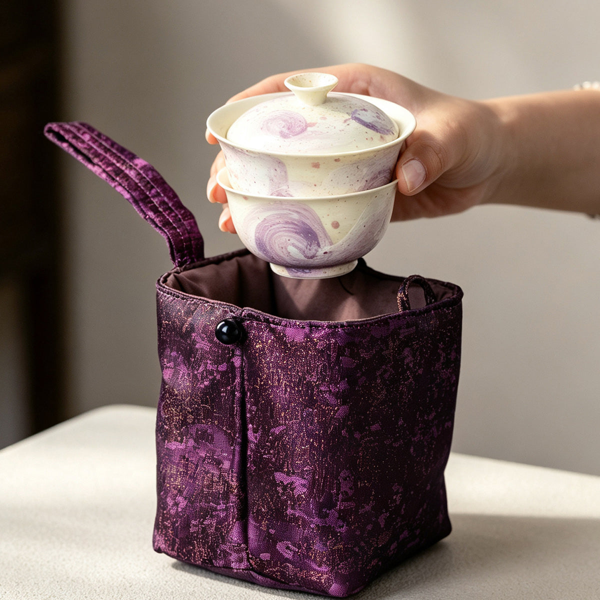 Gaiwan and cup stacked and lowered into the purple travel pouch