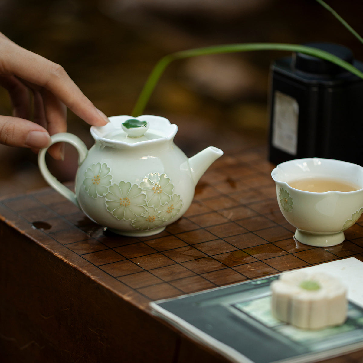 Chrysanthemum porcelain tea cup beside the matching teapot on a wooden tea table