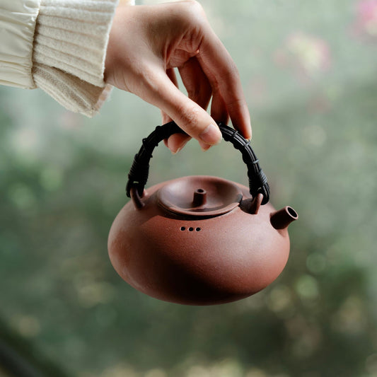 Rattan handle clay boiling teapot 420ml held up by its overhead handle