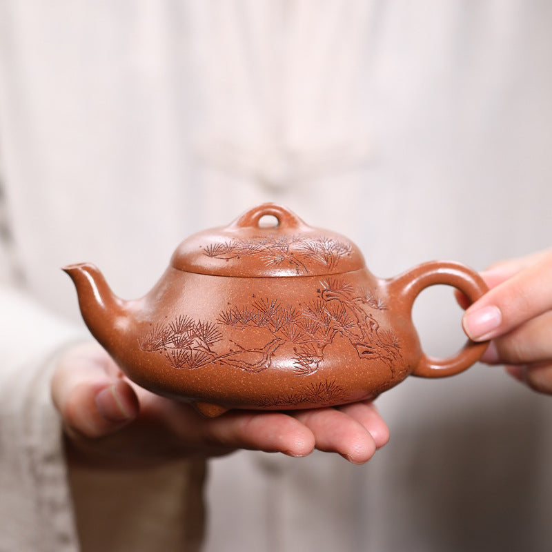 Pine Wind Yixing teapot held in one hand, showing the carved pine branch and its 240ml size against the palm