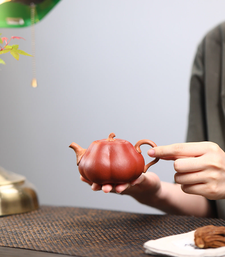 The Pumpkin Yixing clay teapot resting in an open palm with a finger on the vine-shaped side handle