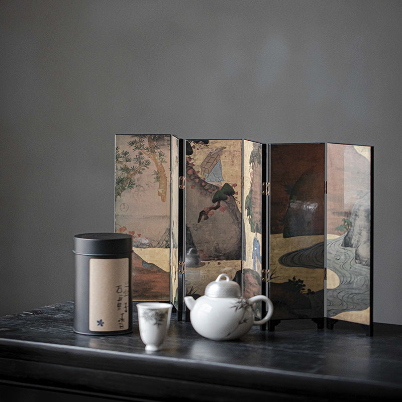 Gold Meadow mini folding screen, reverse mountain scene, standing behind a black tea canister, cup and white teapot