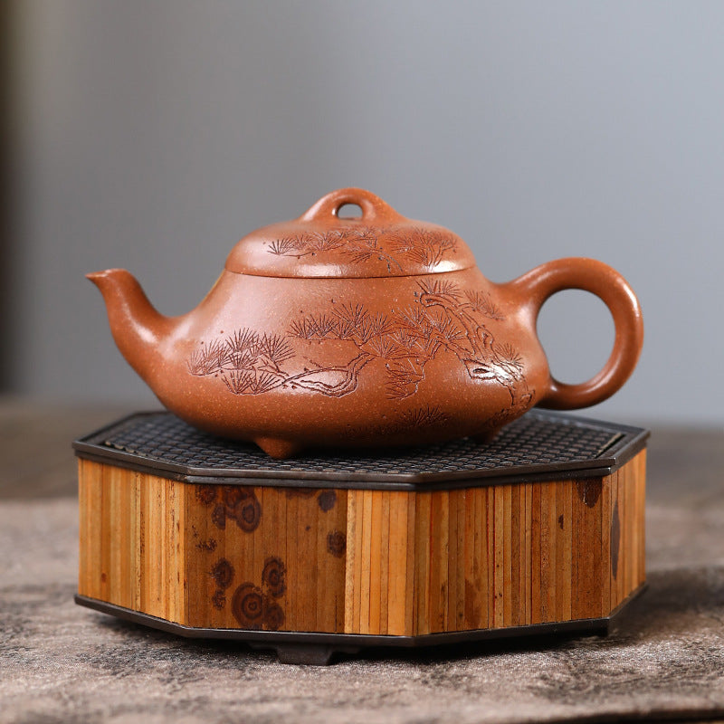 Pine Wind Yixing teapot on a bamboo tea stand, hand-carved pine across the full round body