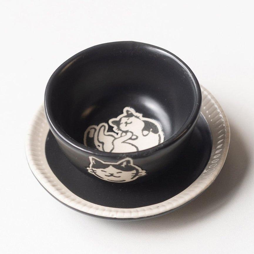 Black cat cup and saucer set with the large cup on its saucer beside a black plate