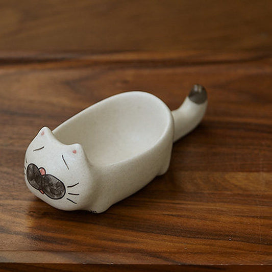 Sleepy cat chopstick rest dish, matte off-white ceramic, on a walnut board