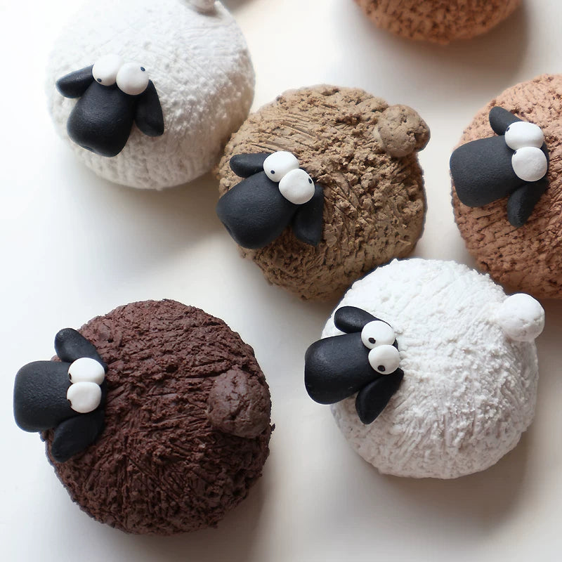 Handmade pottery sheep tea pets in white, khaki and brown clay, lined up on a white background