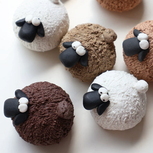 Handmade pottery sheep tea pets in white, khaki and brown clay, lined up on a white background