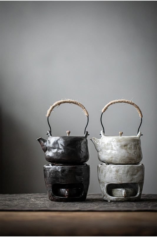 Two ceramic teapots with warmer on stands against a gray background